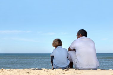 Father and son sitting on the edge of the ocean clipart