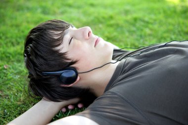 Teenager lying on grass listening to music clipart