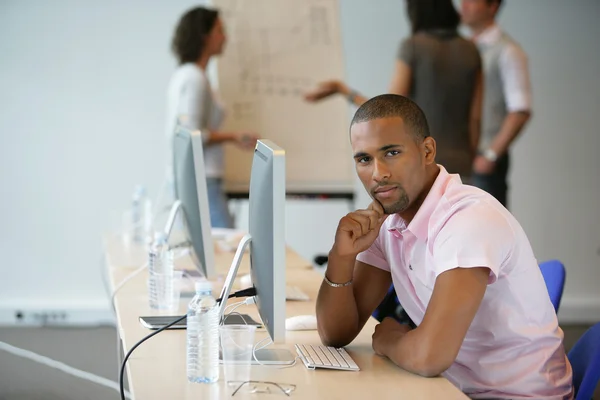 Empresário sentou-se no computador com colegas em segundo plano — Fotografia de Stock
