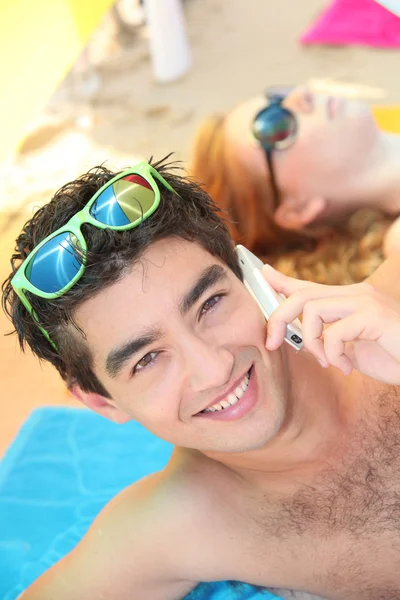 Man som ligger på en strand, med sin telefon — Stockfoto