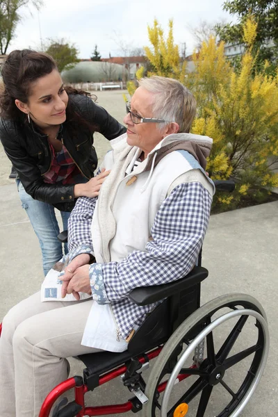 Eine junge Frau hilft einer Seniorin im Rollstuhl — Stockfoto