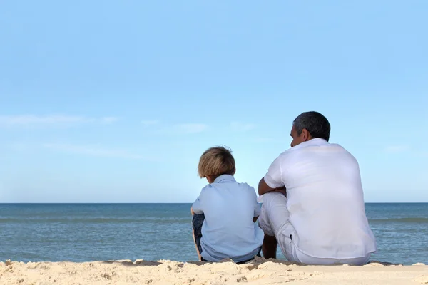 Pai e filho sentados à beira do oceano — Fotografia de Stock