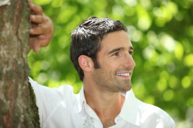Handsome man leaning against a tree clipart