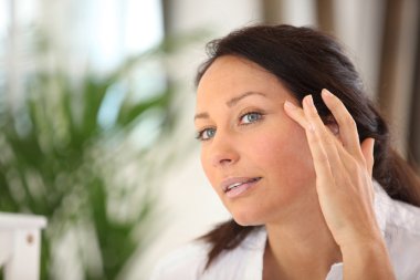 A woman spreading out cosmetic cream on her face clipart