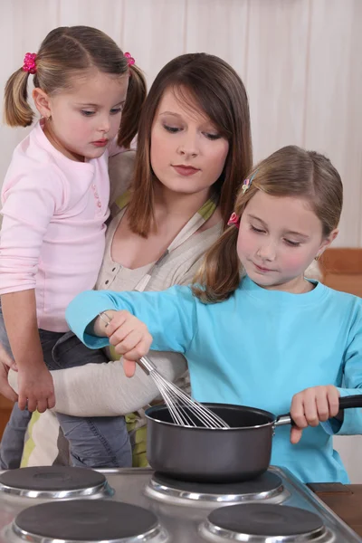 Jovem mulher e meninas preparando um bolo — Fotografia de Stock