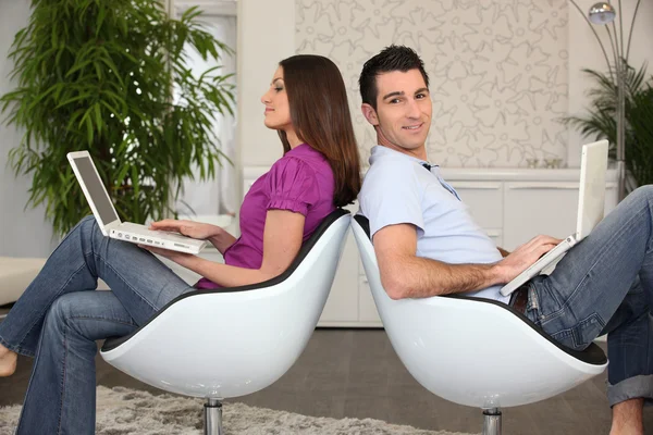 Paar met behulp van laptops in bijpassende stoelen — Stockfoto