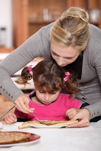 小さな女の子にパンケーキを与える母 — ストック写真