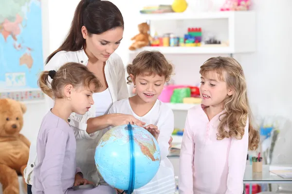 Uma mulher e três meninas observando um globo — Fotografia de Stock