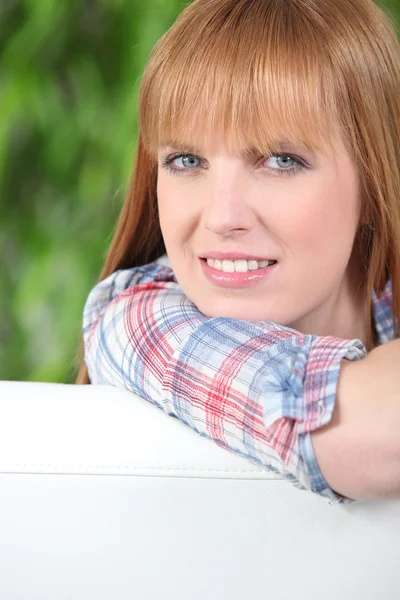 Redheaded woman leaning on the back of a white sofa — Stock Photo, Image