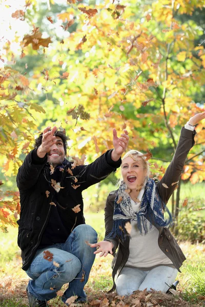 Joyful couple playing with dead leaves in autumn — Stock Photo, Image