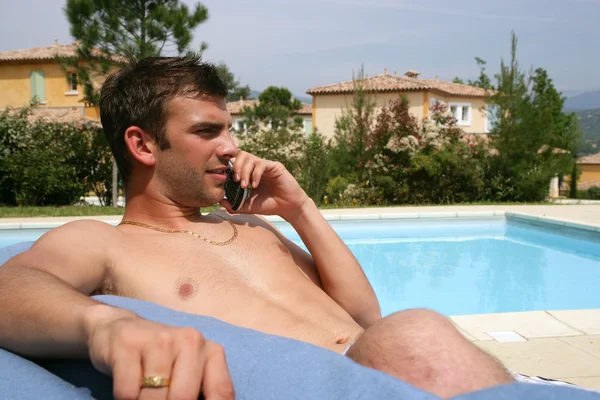 Homem sentado junto à piscina com telefone móvel — Fotografia de Stock