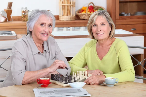 Две пожилые женщины играют в шахматы на кухне — стоковое фото