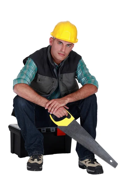 Arbeiter sitzen mit Säge in der Hand auf Werkzeugkiste — Stockfoto
