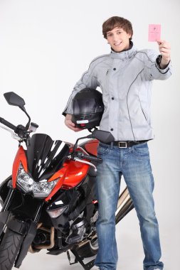 Young man holding driving license stood next to motorcycle clipart