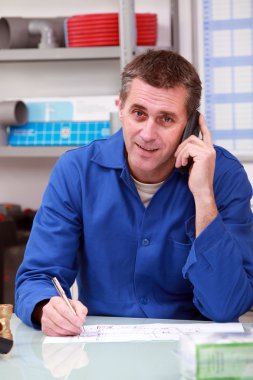 Man in a plumber's merchants taking an order on the telephone clipart