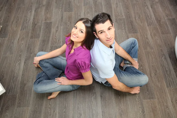 Couple sat back to back on laminate flooring — Stock Photo, Image