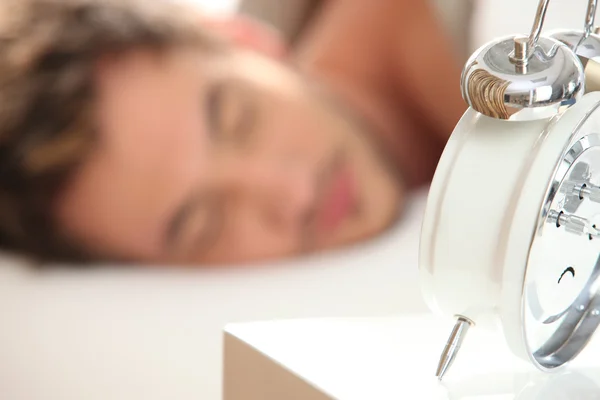 Ung man sover med en väckarklocka i förgrunden — Stockfoto