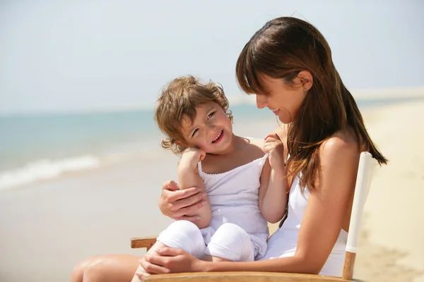 Mother and daughter sat on chair at the beach — Stock Photo, Image