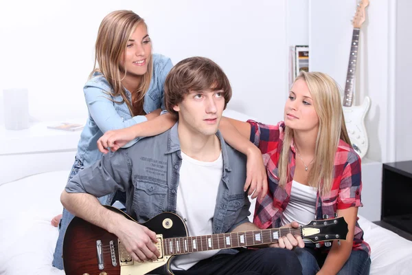 Teenage boy playing electric guitar next to two girls — Stock Photo, Image