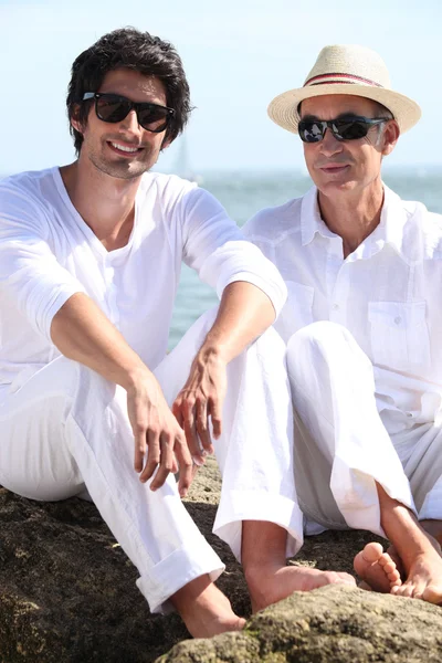 父亲和儿子在海滩上坐在岩石上 — 图库照片