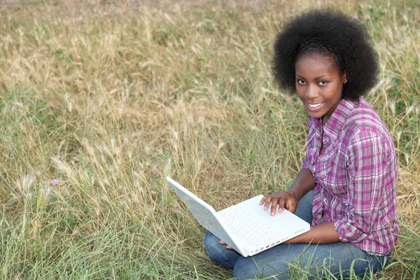 年轻的美国黑人女子坐在草丛中与她的笔记本电脑 — 图库照片