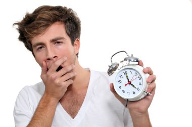 Yawning man holding alarm clock clipart