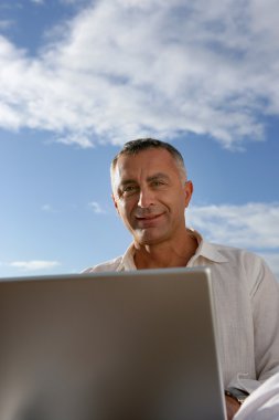 Mature man working outdoors with laptop clipart