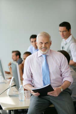 Senior manager sitting on a desk in front of his team clipart