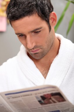 Handsome man in a toweling robe reading a journal clipart