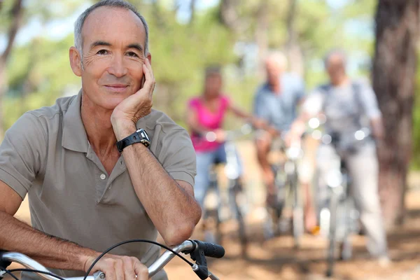 Senior on a bike with friends in the background — Stock Photo, Image