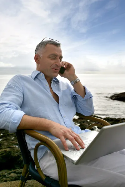 Mann benutzt seinen Laptop draußen und telefoniert — Stockfoto