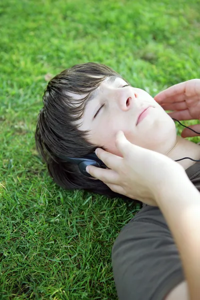 草の上に置いたヘッドフォンで音楽を聞いている少年のポートレート — ストック写真