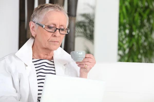 Mulher sênior com computador portátil beber café — Fotografia de Stock