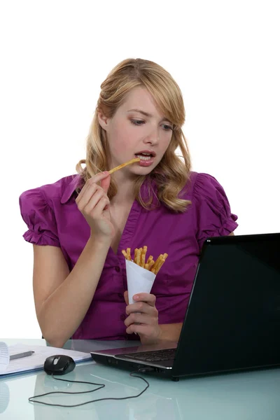 Žena úředník jíst hranolky u svého psacího stolu — Stock fotografie