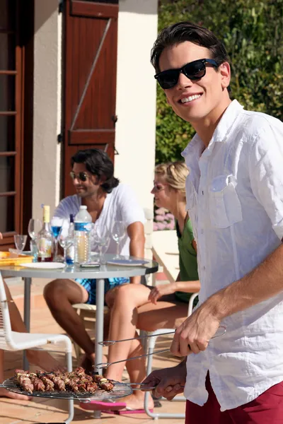 stock image Young man cooking kebabs on a barbecue for friends