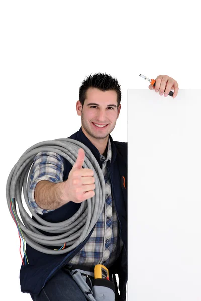 Young electrician all smiles carrying hose and board — Stock Photo, Image