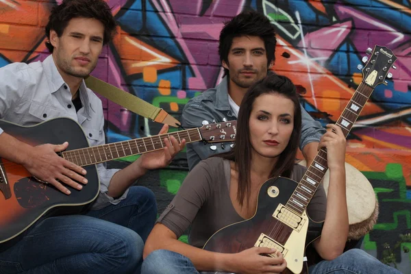 Zwei junge Männer und eine junge Frau spielen Gitarre und Djembe vor einem T-Shirt — Stockfoto