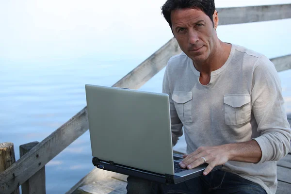 Man using a laptop computer by the water — Stock Photo, Image