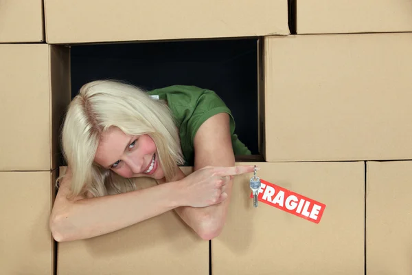 Mujer rodeada de paquetes sosteniendo una llave y sonriendo — Foto de Stock