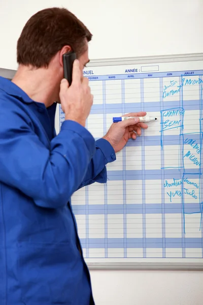 Trabalhador manual escrevendo nomes em um planejador de parede — Fotografia de Stock