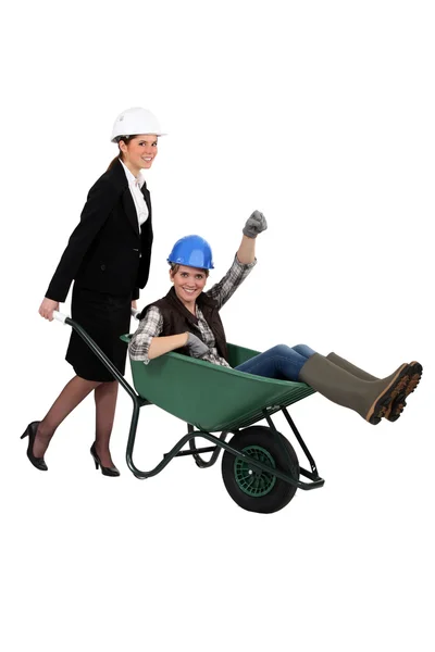 Mulher empurrando colega de trabalho no carrinho de mão — Fotografia de Stock