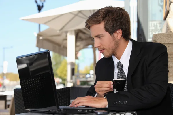 Uomo d'affari bere caffè e guardare il suo computer portatile in un caffè di strada — Foto Stock