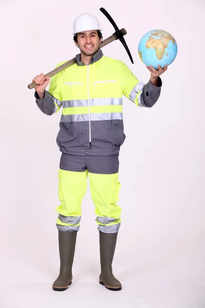 Trabalhador segurando um globo e uma picareta — Fotografia de Stock