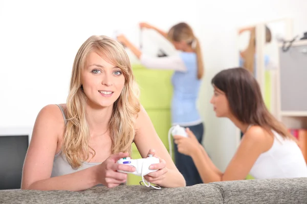 Två väninnor som spelar TV-spel med andra vän i bakgrunden — Stockfoto