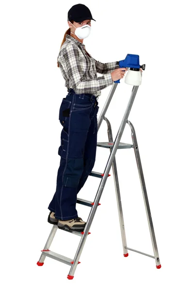 Een vrouwelijke schilder met een spuitpistool op een ladder. Stockafbeelding
