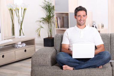 Man using a laptop computer in his front room clipart