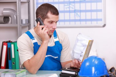 Plumber checking a part on the telephone clipart