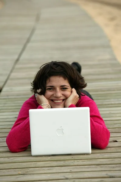 Mujer joven acostada en la playa con su portátil —  Fotos de Stock