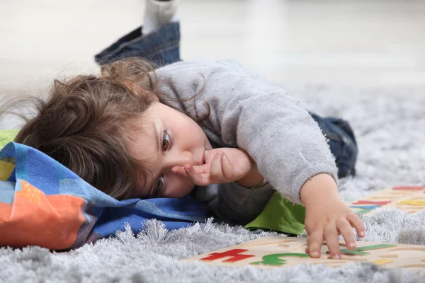Criança deitada no chão brincando com um quebra-cabeça — Fotografia de Stock
