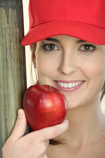 Mulher usando um boné e comendo uma maçã — Fotografia de Stock